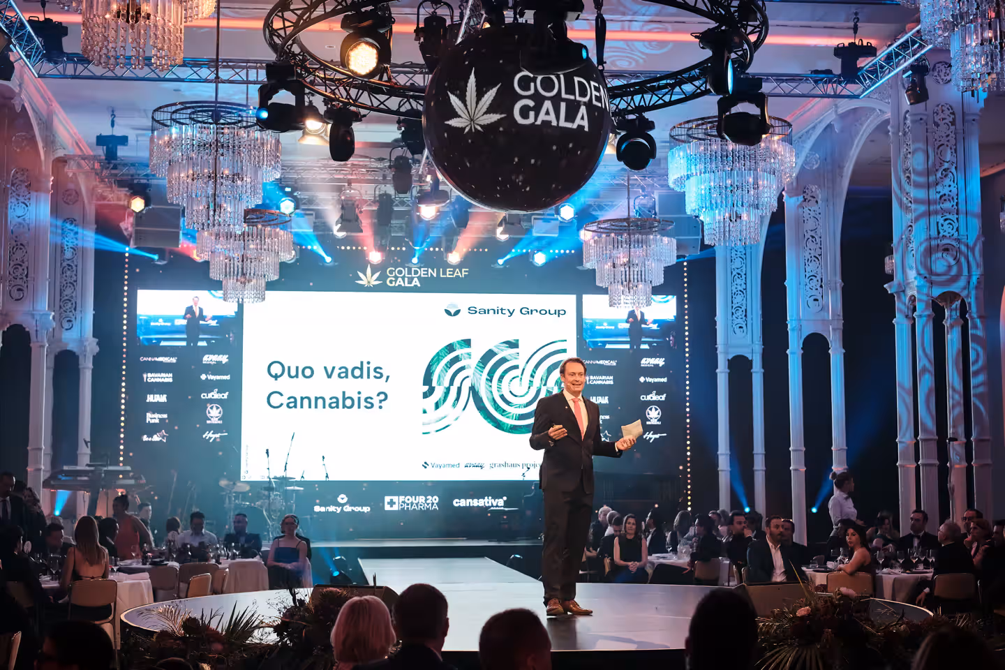 Mann hält Rede auf der Golden-Gala-Veranstaltung mit Cannabis-Thema und moderner Lichtinstallation