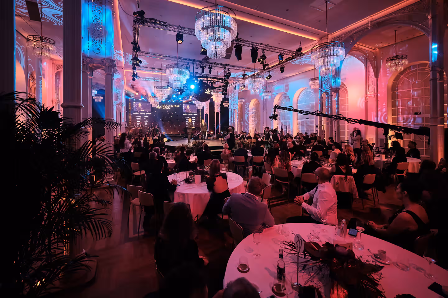 Großes Publikum bei einem Event in einem prächtig beleuchteten historischen Saal mit Live-Musik und Gästen an Tischen