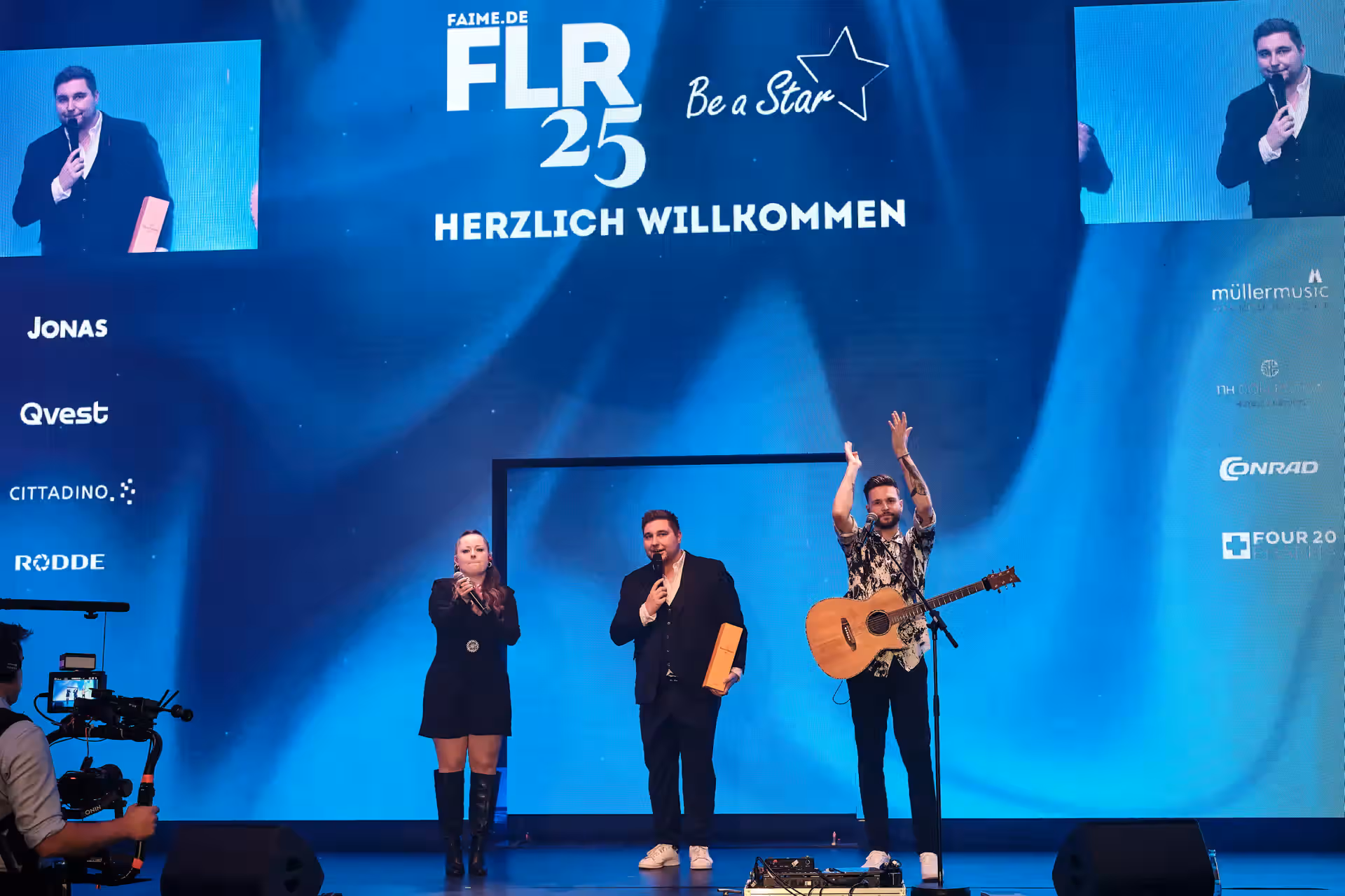 Drei Personen stehen auf einer Bühne mit Mikrofonen und präsentieren ein Event unter dem Motto FLR 25 Be a Star
