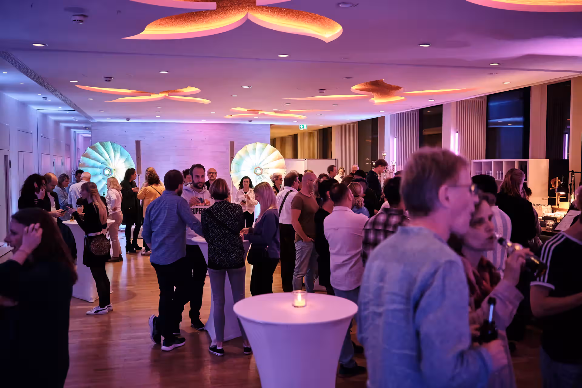 Grosse Gruppe Menschen bei einer Abendveranstaltung mit Lichterinstallation und DJ-Pult im Hintergrund