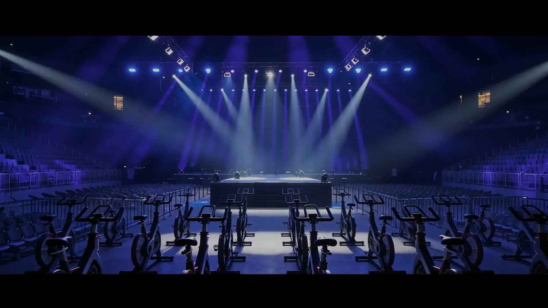Leere LANXESS arena in blauem Licht, davor Reihen von Indoor-Bikes vor der Bühne.